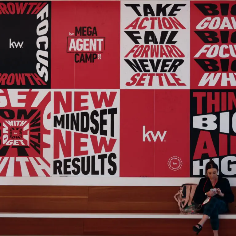 Mega Agent Camp'te Keller Williams sloganlarıyla kaplı duvarın önünde oturan danışman