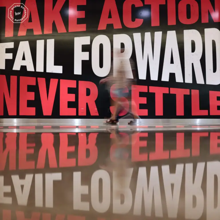Keller Williams etkinliğinde "Take Action, Fail Forward, Never Settle" yazılı dev pano
