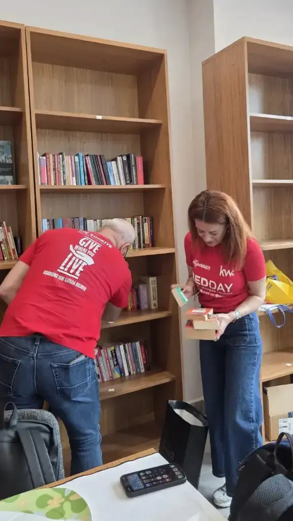 RED DAY gününde kütüphane raflarını düzenleyen kırmızı tişörtlü KW danışmanları