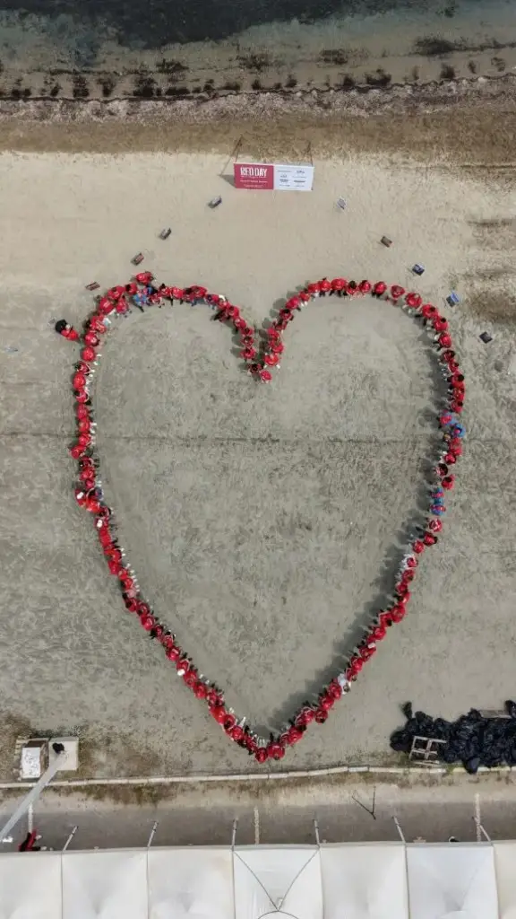RED DAY gününde sahilde kalp şekli oluşturan kırmızı tişörtlü KW danışmanları, havadan çekim
